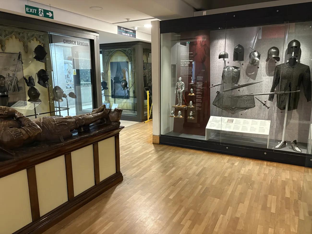 A fake stone effigy of a knight from the high medieval era. Next to the effigy are glass cases with medieval arms and armour.
