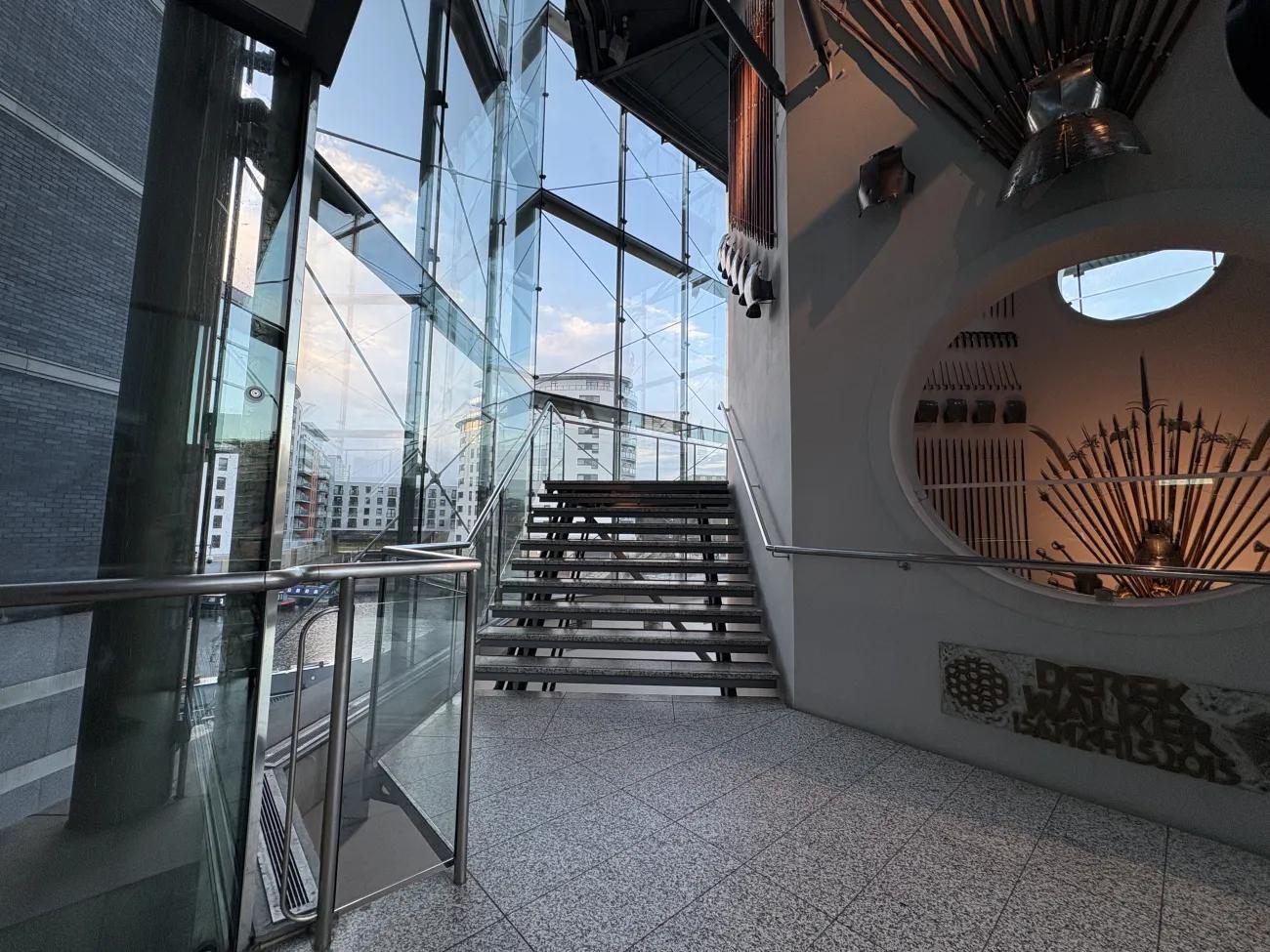 A simple stone and steel staircase with a concrete wall on one side and a clear glass wall on the other.