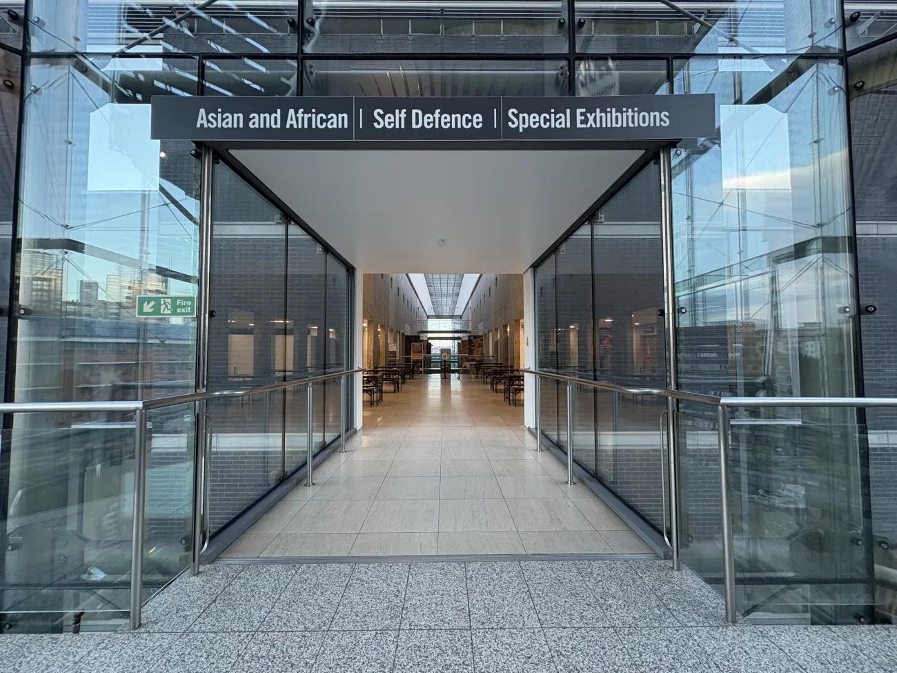 An entrance way of steel and glass leading to a wider picnic area with colourful chairs.