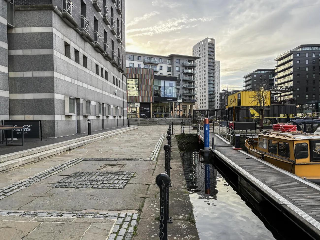 A flagstone-paved path between a high walled grey building and a body of water.