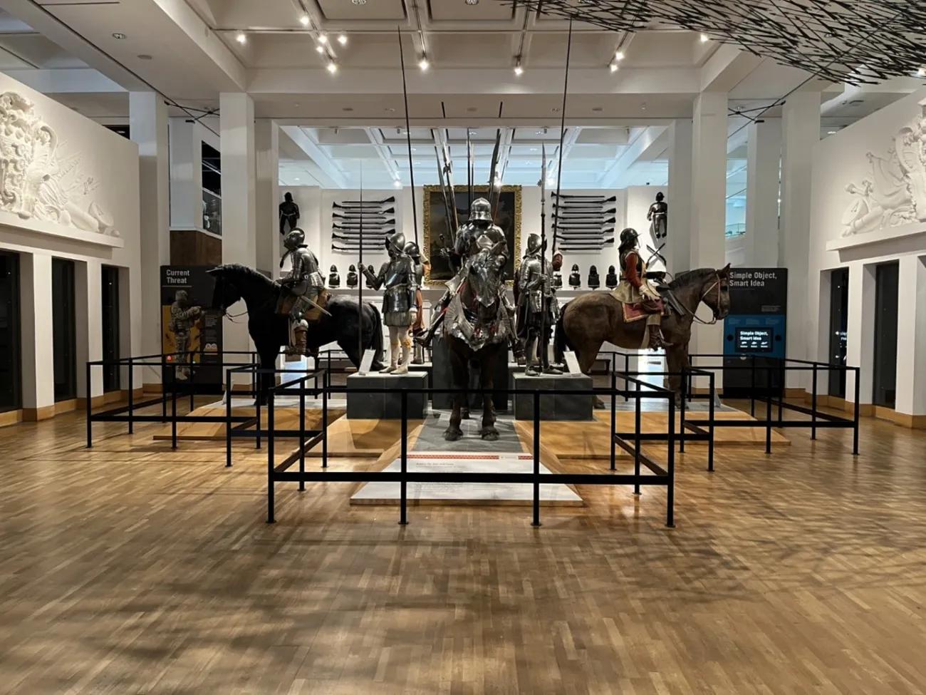 A photo of a display of armour with mannequins on horseback and on foot forming a cross on the floor