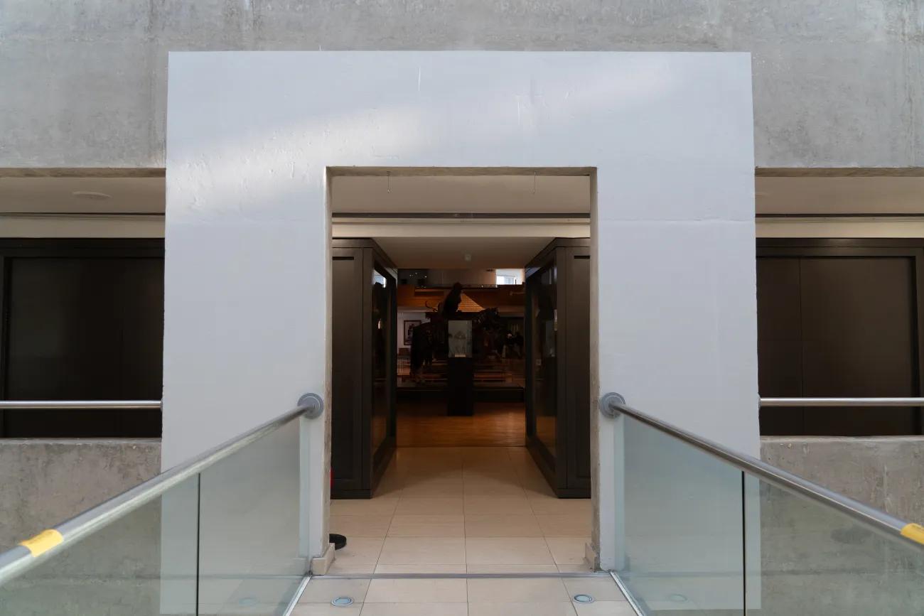 The entrance to a museum gallery is in darkness, framed by a square white archway