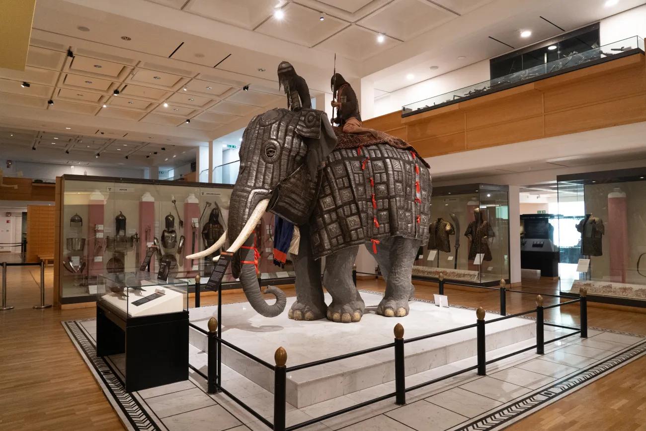An open plan room with glass cases displaying Japanese and Indian armour surrounds a life size model of elephant armour