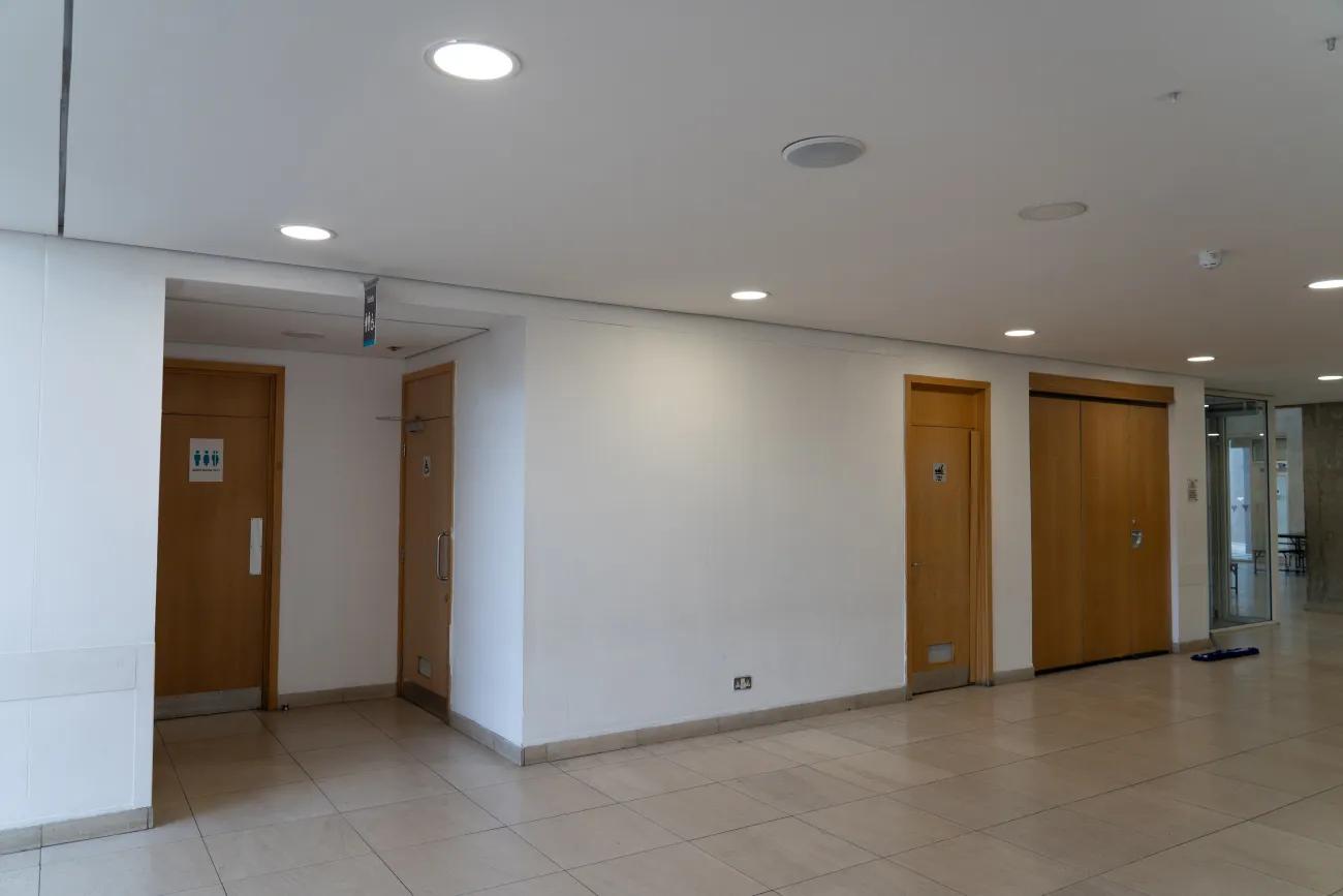 A blank white wall features plain light brown doors leading to rest rooms