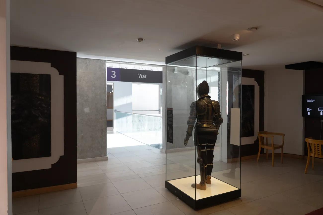 A suit of armour in a glass case looking out onto the entrance of the gallery