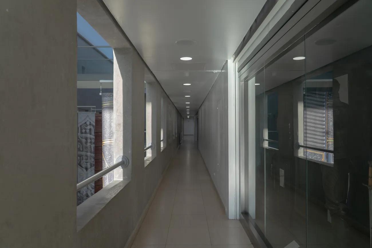 A plain corridor with beige flooring and grey concrete balconies punctuating one side.