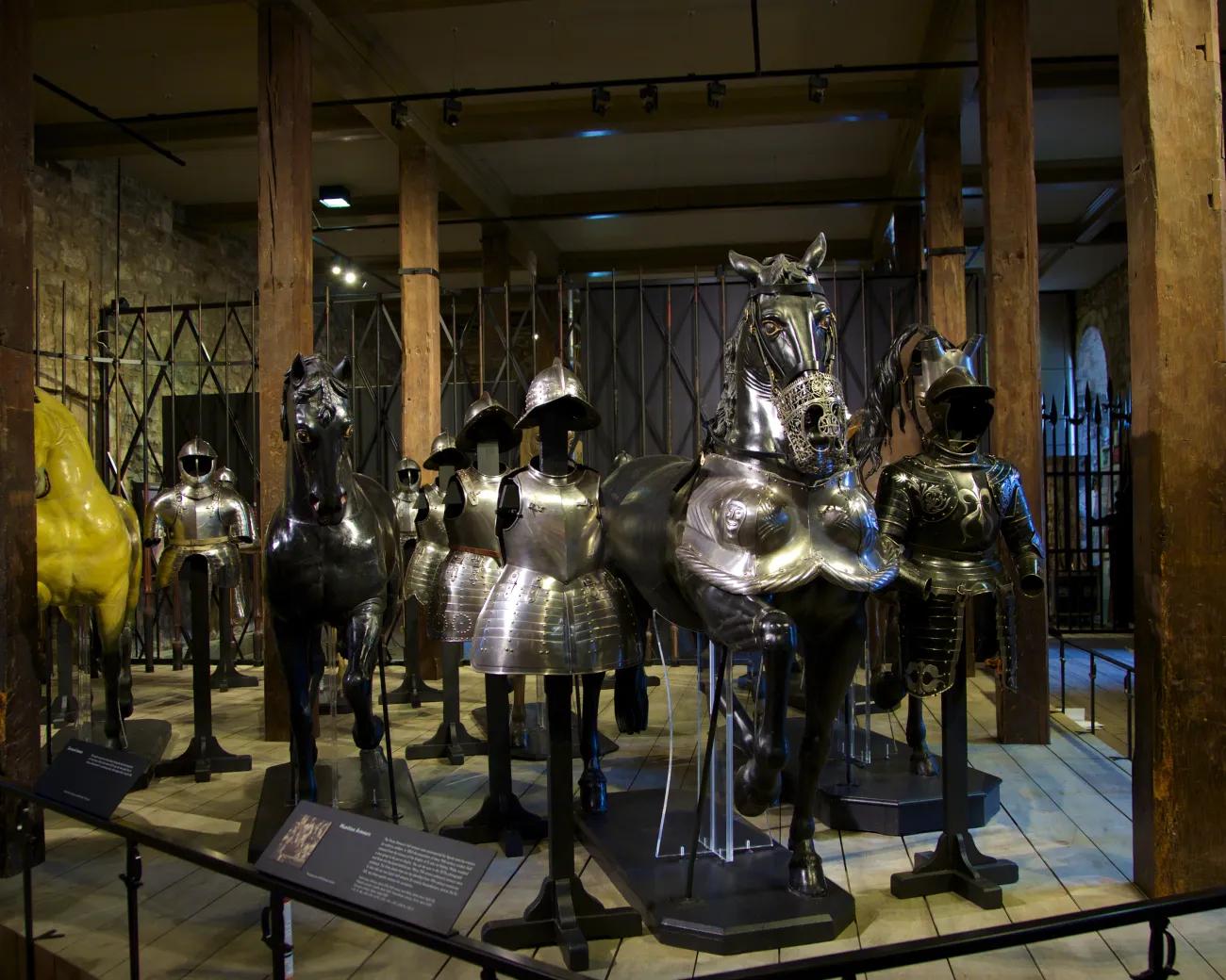 An interior photograph of the White Tower at the Tower of London, showing sets of armour, both human and horse, arranged around informative panels