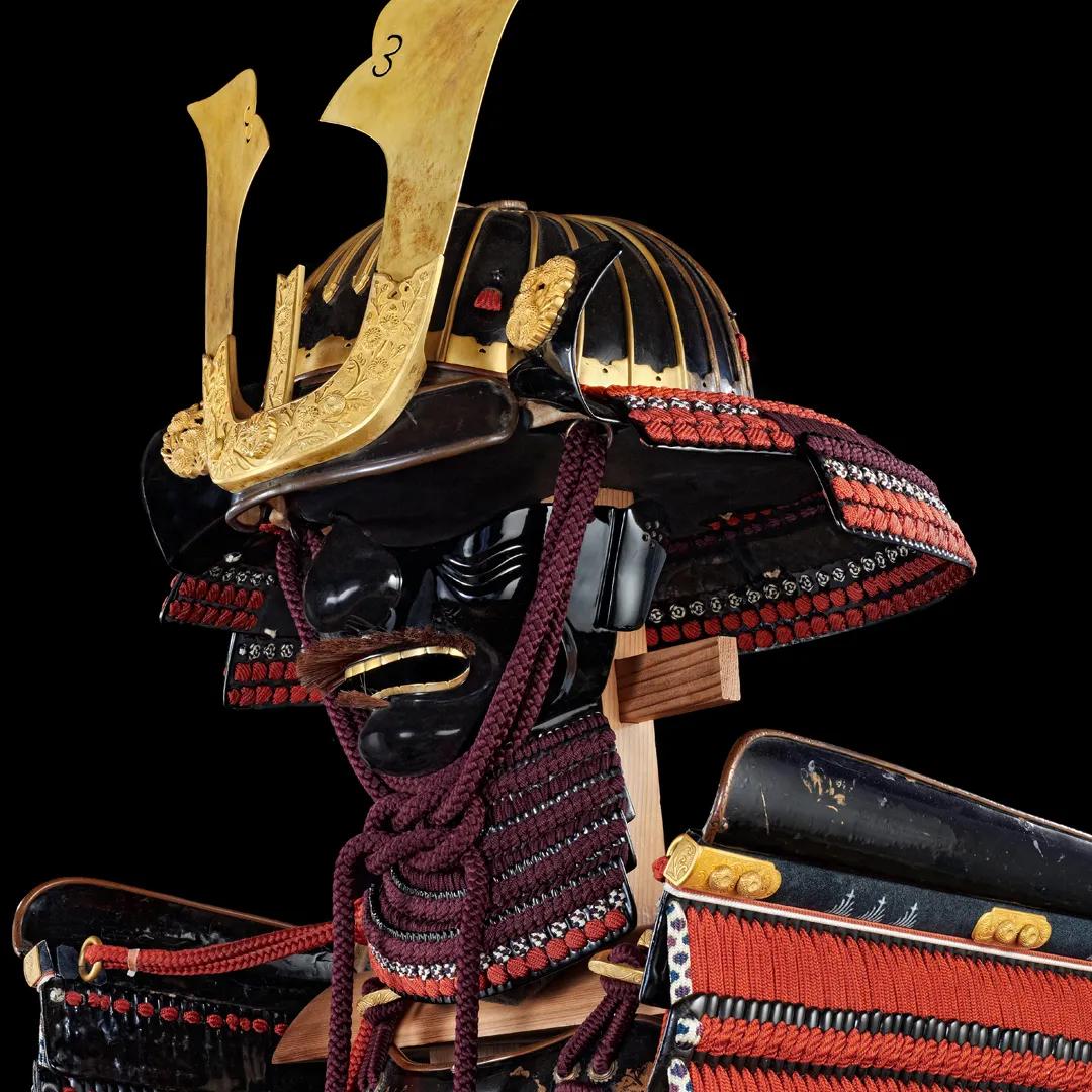 The kabuto helmet of a suit of lacquered Japanese armour in black and red. The background is black.