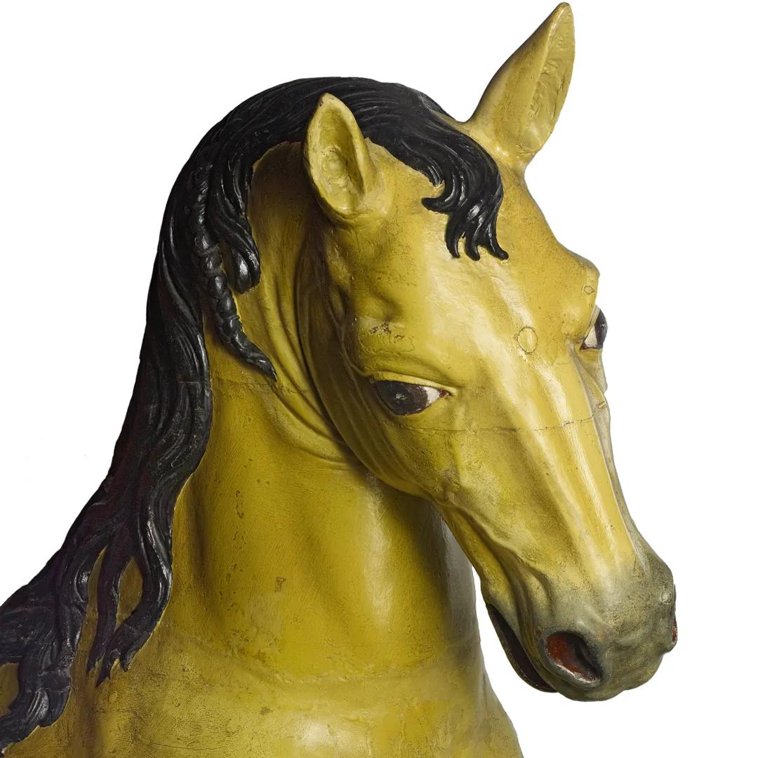 A carved wooden horse with yellow skin and black mane