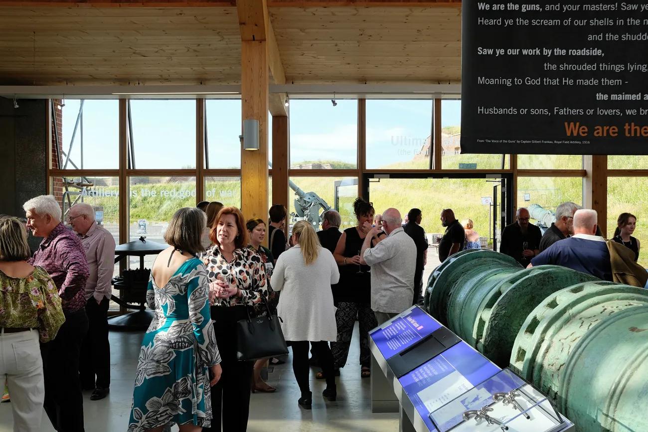 Visitors gather in a museum gallery with historic artillery displays, large windows and interpretive panels