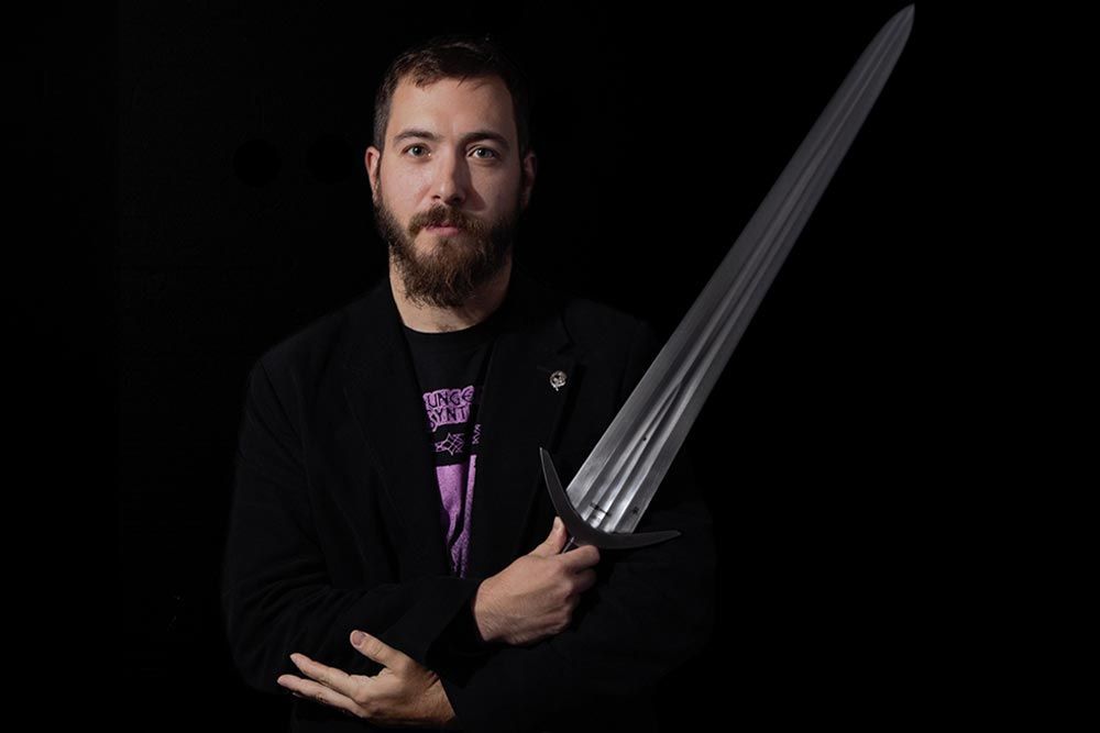 Iason-Eleftherios Tzouriadis on a dark background holding a Windlass Cinquedea sword