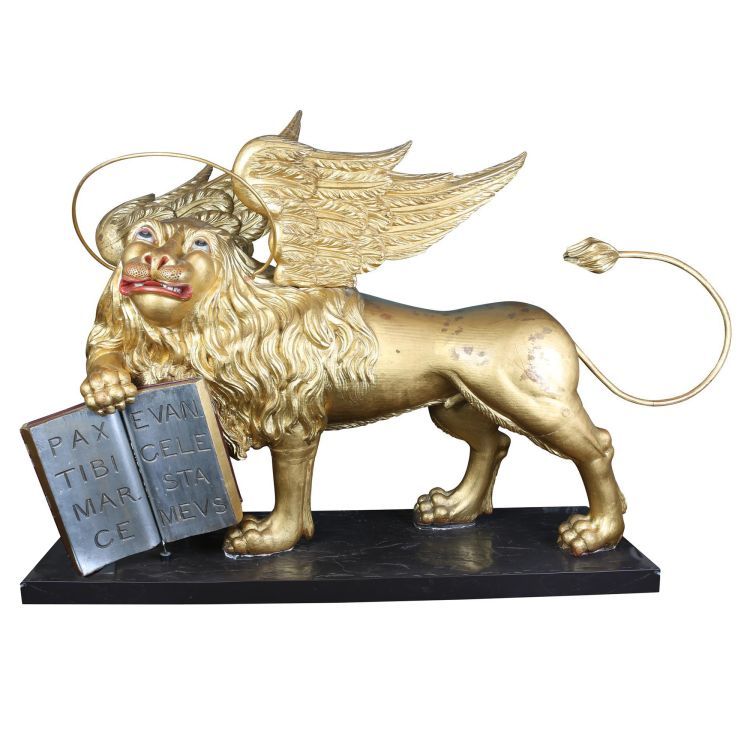 A statue of a golden winged lion holding a book in its front right paw