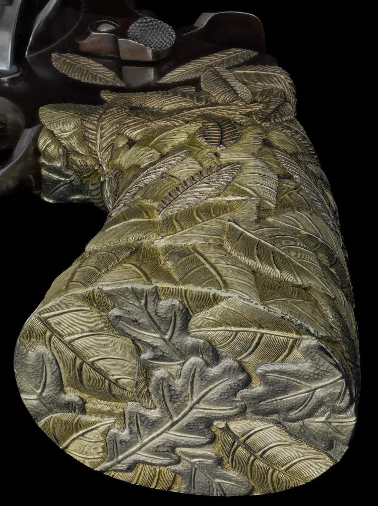 A close up of a revolver stock decorated in gold leaf on a black background