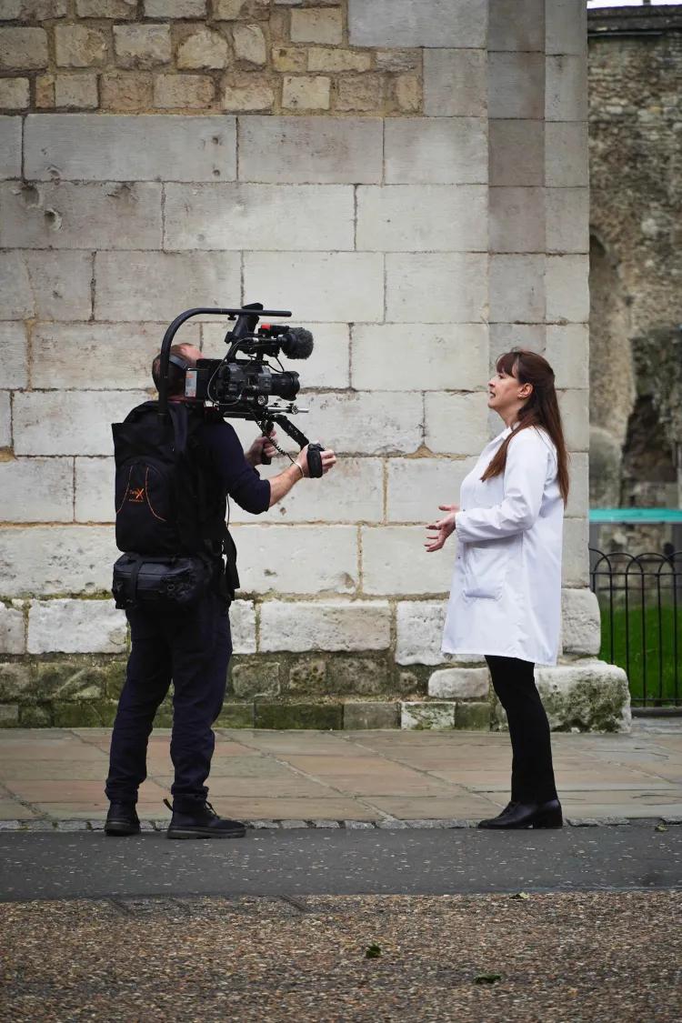 Curator Emma Mawdsley being filmed by man with camera on his shoulder.
