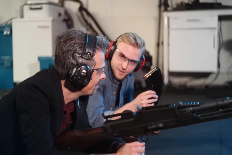 Jonathan Ferguson and Luke Tomes wearing ear defenders in discussion with Jonathan holding a bren gun