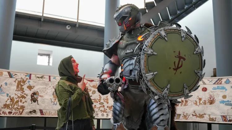 Doom character and museum visitor looking at each other in front of the layeaux Tapestry in the Hall of Steel