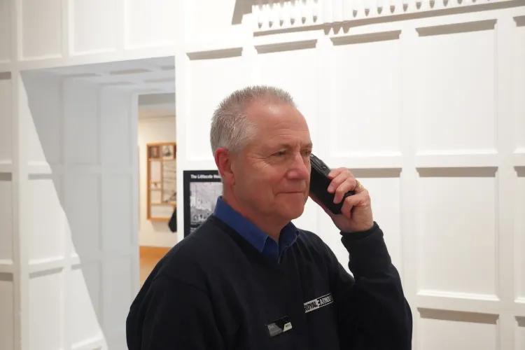 A man in a dark blue jumper stands with a walkie talkie