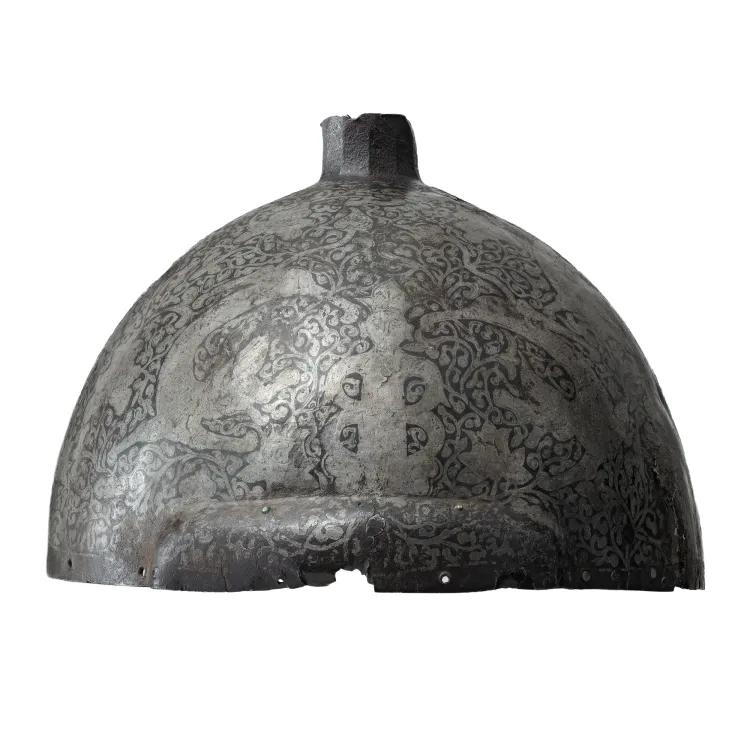 A hemispherical metal helmet engraved with silver leaves and human figures.