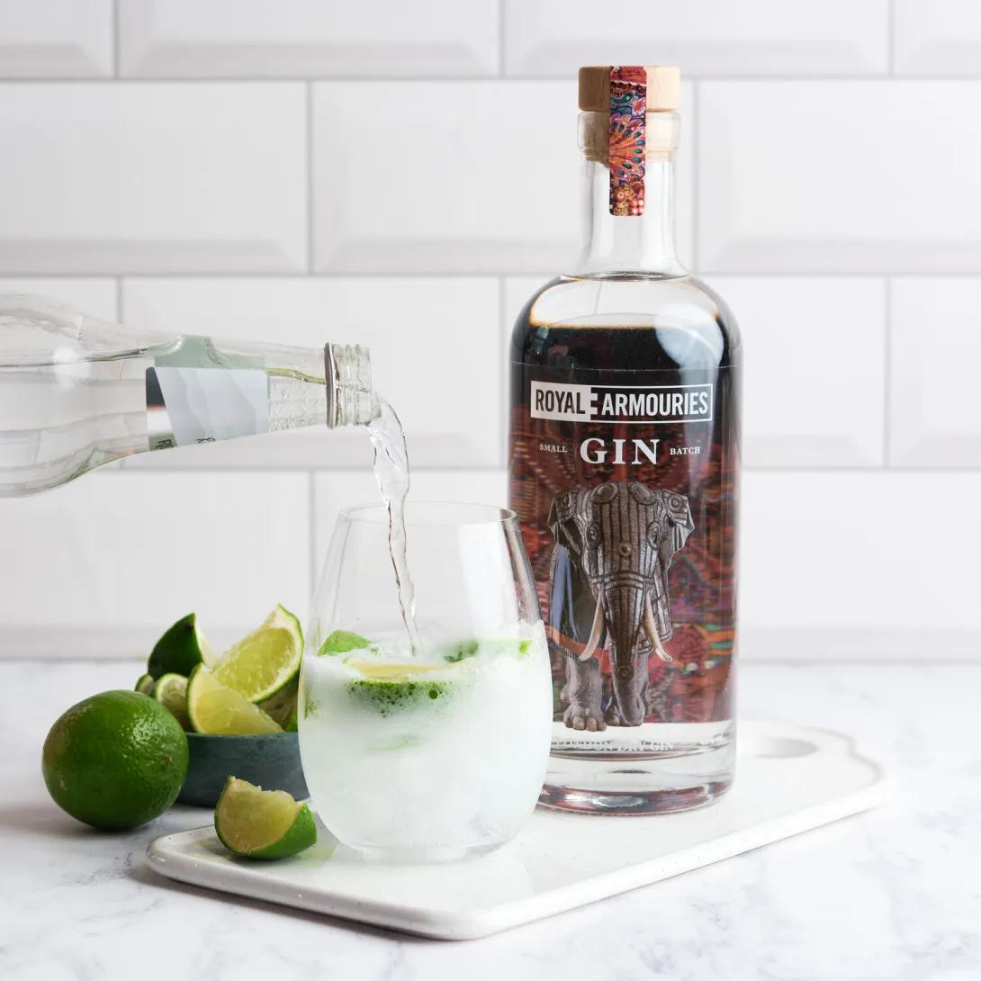 Royal Armouries GIN next to tonic being poured into glass with sliced limes.