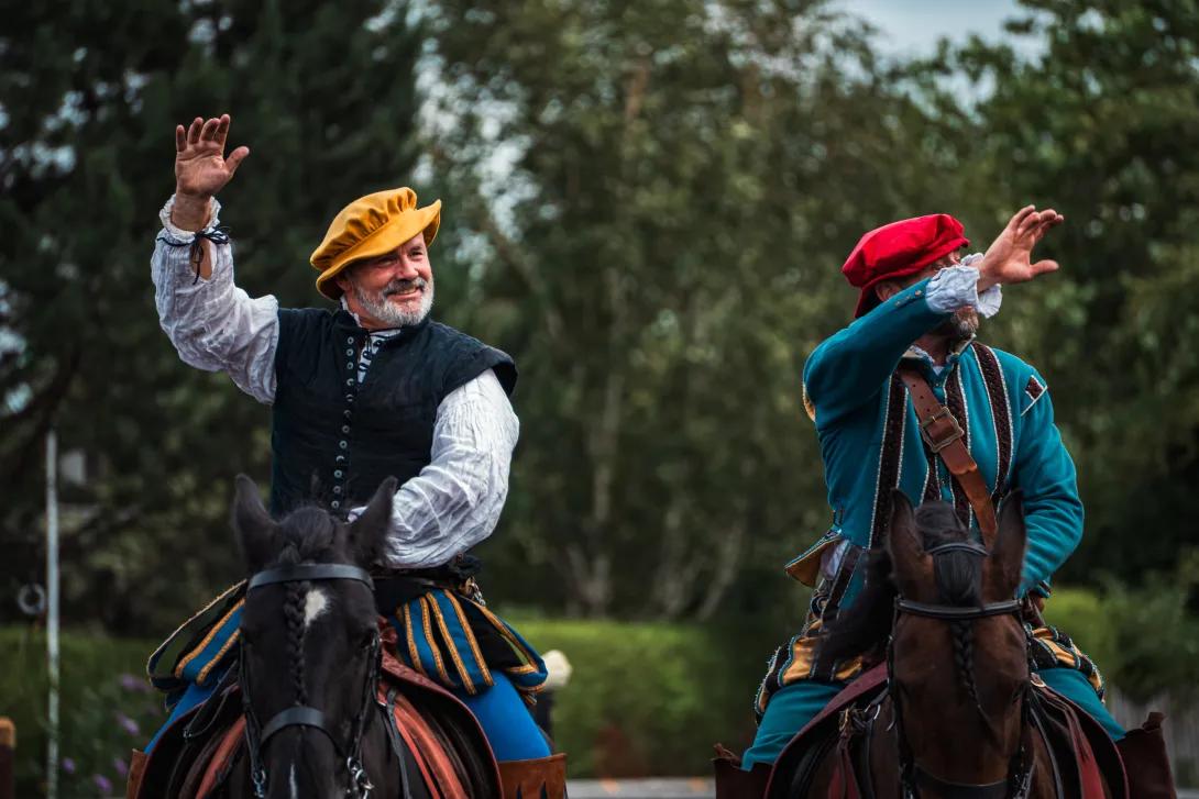 Two jousters on horseback waving at crowd